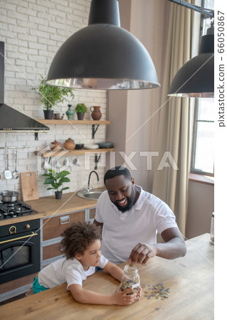 Dark-skinned bearded man putting coins into the moneybank and smiling Dark-skinned bearded man putting coins into the moneybank and smiling 66050867