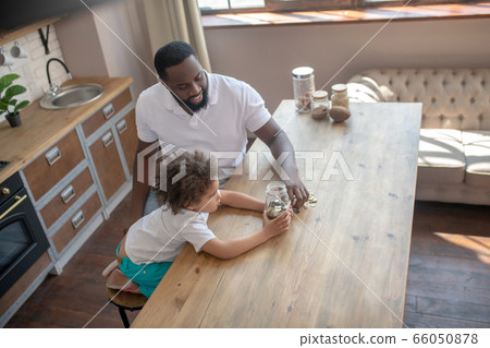 Dark-skinned bearded man talking to his son about saving money 66050878