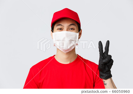 Covid-19, self-quarantine online shopping concept. Asian courier staying positive, friendly showing peace sign in medical mask and gloves, measures for safe order deliver on self-quarantine Covid-19, self-quarantine online shopping concept. Asian courier staying positive, friendly showing peace sign in medical mask and gloves, measures for safe order deliver on self-quarantine 66050960