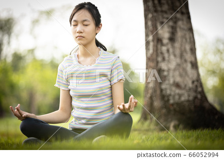 Happy woman meditating in yoga pose or lotus position on the green grass under the tree at park,asian child girl practicing yoga meditation in nature outdoor,relax time,calmness,meditation,health care 66052994