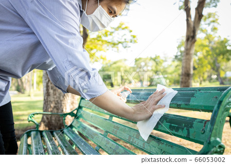 Asian woman in a mask,spraying alcohol,wiping the dirt,disinfectant spray on bench,during the pandemic of Covid-19,Coronavirus,cleaning,disinfecting wipe the public bench at park,hygienic and safety 66053002