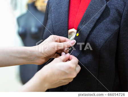 Female hands with a jacket and a pin, close up. Tailor makes a fitting on mannequin, selective focus. 66054726