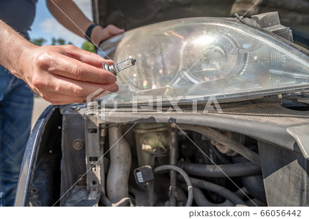 The man changes the bulb in the headlight of a car 66056442