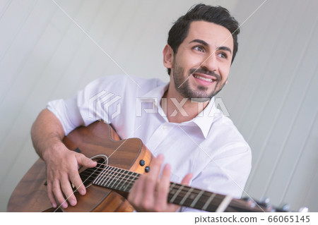 Happy man playing guitar while sitting on sofa in living room, Enjoying carefree time at home. 66065145