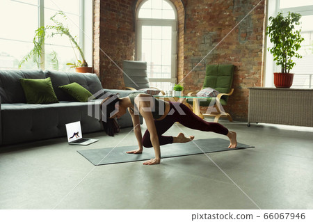 Sporty young woman taking yoga lessons online and practice at home Sporty young woman taking yoga lessons online and practice at home 66067946