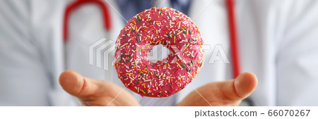 Doctor in office holding in hand pink doughnut 66070267