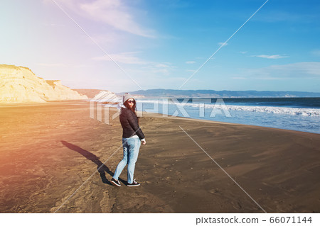 Woman in a hat walking on Pacific ocean coast on windy day Woman in a hat walking on Pacific ocean coast on windy day 66071144