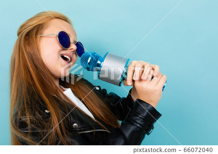 attractive european girl in a leather jacket in sunglasses singing with a microphone on a light blue attractive european girl in a leather jacket in sunglasses singing with a microphone on a light blue 66072040