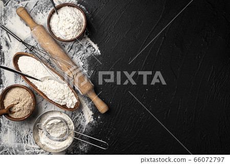 Different types of flour in wooden bowls on black table, top view 66072797
