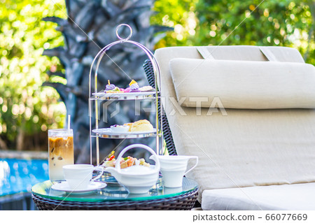 Afternoon tea set with latte coffee and hot tea on table neary chair around swimming pool 66077669