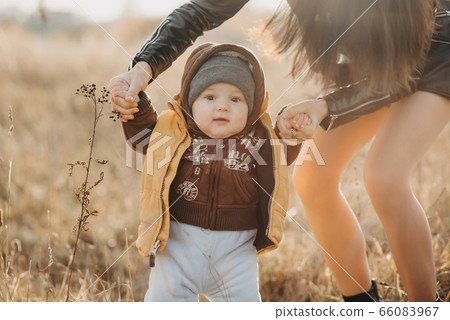 mom holds her baby boy by the hands for a walk. Baby's first steps mom holds her baby boy by the hands for a walk. Baby's first steps 66083967