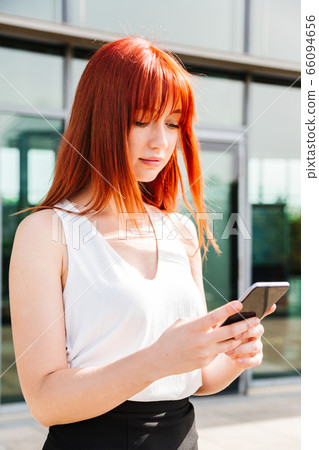 Portrait of red-haired girl using her mobile phone 66094656