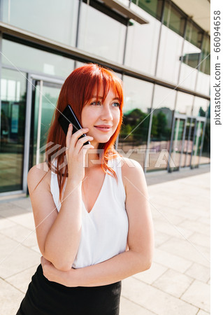 Red-haired girl talks on phone and looks at camera 66094658