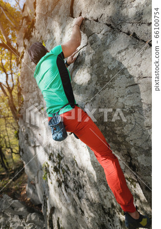 A man is training in free climbing on a rock stone in the forest on a sunny day. The concept of leisure activities of an active lifestyle of people aged A man is training in free climbing on a rock stone in the forest on a sunny day. The concept of leisure activities of an active lifestyle of people aged 66100754