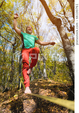 A bearded man aged balancing on a slackline in the autumn forest on a sunny day. The concept of sports leisure at the age of forty 66100761