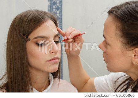 Makeup artist glues bunches on the eyelashes model. 66100866