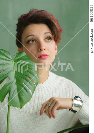 Beauty portrait of sensual brunette girl with dark pink hair and white sweater holding a green spring plant. Beauty, natural cosmetics concept. 66103035