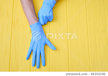 Blue Nitrile gloves. Hands of a medic in the blue latex gloves on a yellow wooden background with place for your text 66103290