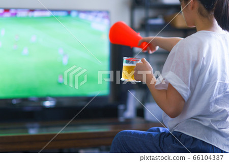 Image of a young woman watching sports at home on TV [Professional soccer video distribution service] 66104387