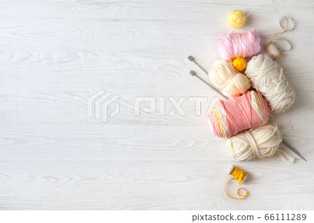Woolen and cotton bright yarn lies in a basket. Glasses lie on a white wooden background. Woolen and cotton bright yarn lies in a basket. Glasses lie on a white wooden background. 66111289