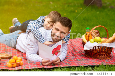Celebrating Father Day. Young father excited to read his son's greeting card during picnic in countryside Celebrating Father Day. Young father excited to read his son's greeting card during picnic in countryside 66111524