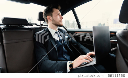 Young businessman using his laptop in luxury car 66111568