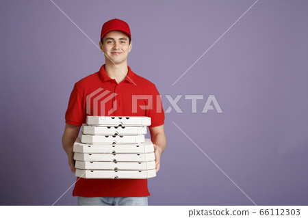 A lot of pizza for big company. Smiling courier holds many boxes 66112303