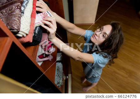 Girl hides a small stack of euro banknotes in clothes in a wardrobe Girl hides a small stack of euro banknotes in clothes in a wardrobe 66124776