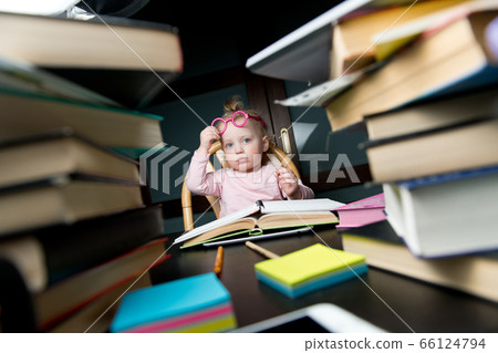 A little student sits at a table that is littered with educational materials A little student sits at a table that is littered with educational materials 66124794