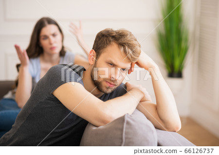 Young bearded man sitting with a depressed look while his wife talking Young bearded man sitting with a depressed look while his wife talking 66126737