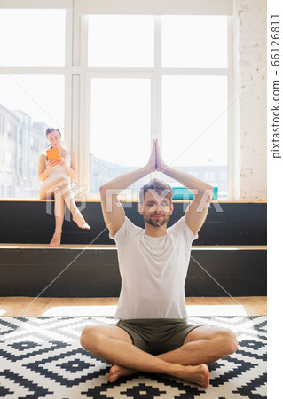 Bearded man in white tshirt sitting on the floor and meditating with his arms up 66126811