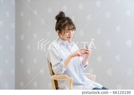 一個女人坐在經典的椅子上,看著智能手機(微笑) 一個女人坐在經典的椅子上,看著智能手機(微笑) 66128190