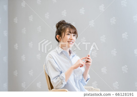 一個女人坐在經典的椅子上,看著智能手機(微笑) 一個女人坐在經典的椅子上,看著智能手機(微笑) 66128191
