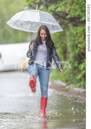 Woman with an umbrella walking in rainboots in a Woman with an umbrella walking in rainboots in a 66130383