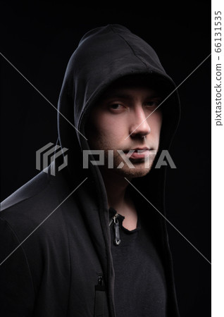 A low-key studio portrait of a large man in a hood sits pondering. Sex faces in the dark hacker stealth and anonymous surveillance hidden concept 66131535