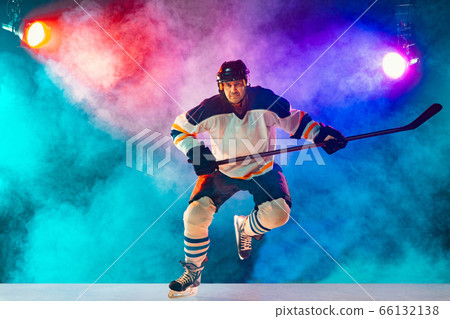 Male hockey player with the stick on ice court and dark neon colored background Male hockey player with the stick on ice court and dark neon colored background 66132138