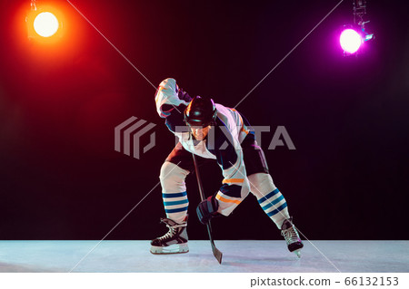 Male hockey player with the stick on ice court and dark neon colored background 66132153