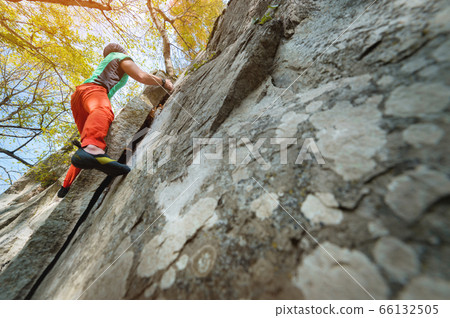 A man is training in free climbing on a rock stone in the forest on a sunny day. The concept of leisure activities of an active lifestyle of people aged 66132505