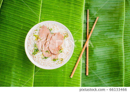 A bowl of Traditional Vietnamese beef soup Pho Bo on banana leaf background. A bowl of Traditional Vietnamese beef soup Pho Bo on banana leaf background. 66133466