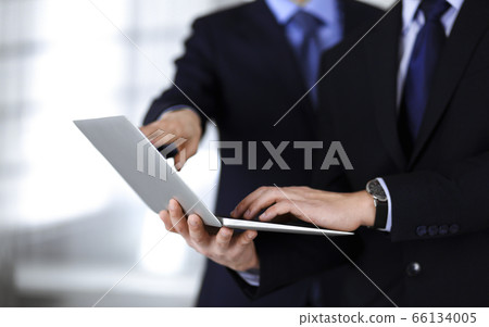 Business people discussing a presentation at meeting, standing in a modern office. Unknown businessman with a colleague search for some information at the laptop, lawyers at negotiation. Teamwork and Business people discussing a presentation at meeting, standing in a modern office. Unknown businessman with a colleague search for some information at the laptop, lawyers at negotiation. Teamwork and 66134005