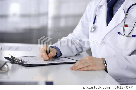 Unknown male doctor sitting and working with clipboard of medication history record in clinic at his working place, close-up. Young physician at work. Perfect medical service, medicine concept 66134077