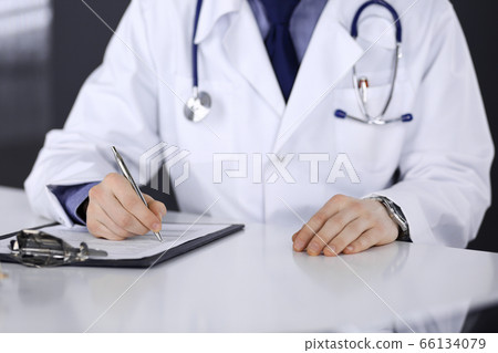 Unknown male doctor sitting and working with clipboard of medication history record in clinic at his working place, close-up. Young physician at work. Perfect medical service, medicine concept 66134079