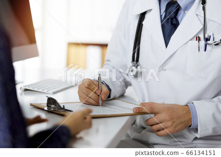 Friendly red-bearded doctor and patient woman discussing current health examination while sitting in sunny clinic. Medicine concept 66134151