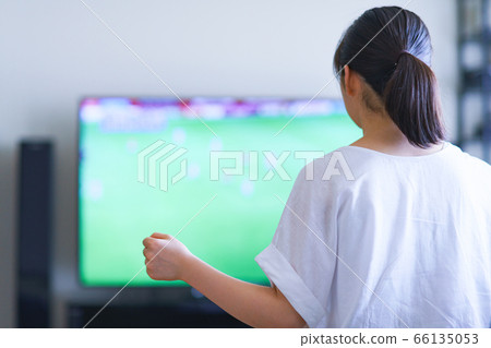 Image of a young woman watching sports at home on TV [Professional soccer video distribution service] 66135053