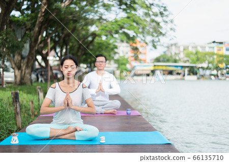 woman practicing yoga and meditation on mat near lagoon with boyfriend. health concept. woman practicing yoga and meditation on mat near lagoon with boyfriend. health concept. 66135710