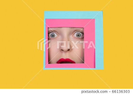 Face of caucasian woman peeking throught square in yellow background Face of caucasian woman peeking throught square in yellow background 66136303