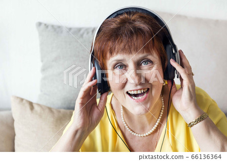white adult woman in headphones listening to music and singing, portrait of a woman close up white adult woman in headphones listening to music and singing, portrait of a woman close up 66136364