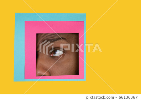 Eye of african-american man peeking throught square in yellow background 66136367
