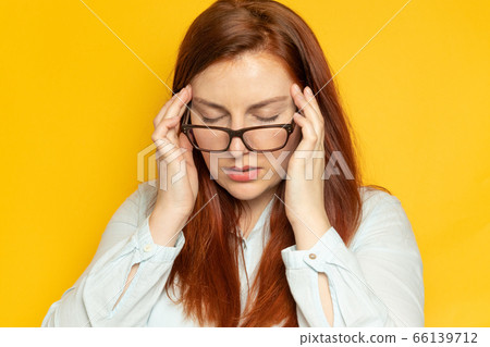 Having a headache concept. Tired woman in a blouse and eyesight glasses with stress on a yellow wall background. Having a headache concept. Tired woman in a blouse and eyesight glasses with stress on a yellow wall background. 66139712