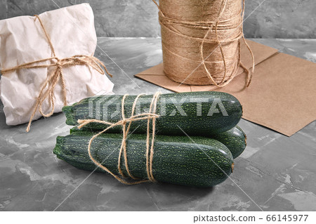 A bunch of zucchini on a gray background with a paper bag for delivery, food delivery, environmental packaging. Copy space, fresh vegetables. A bunch of zucchini on a gray background with a paper bag for delivery, food delivery, environmental packaging. Copy space, fresh vegetables. 66145977